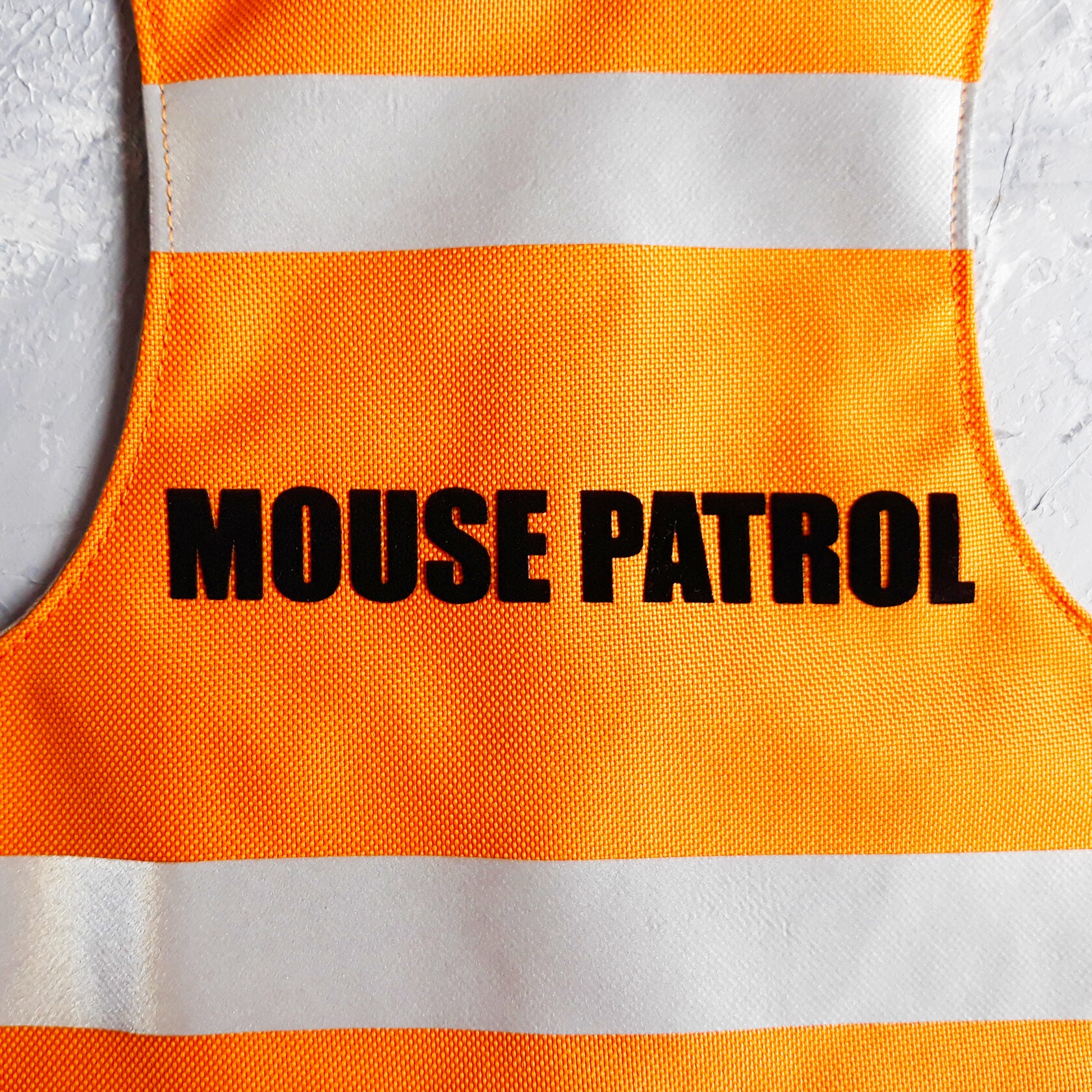 Close-up of a bright orange safety vest with horizontal reflective white stripes and the text "MOUSE PATROL" in black capital letters.