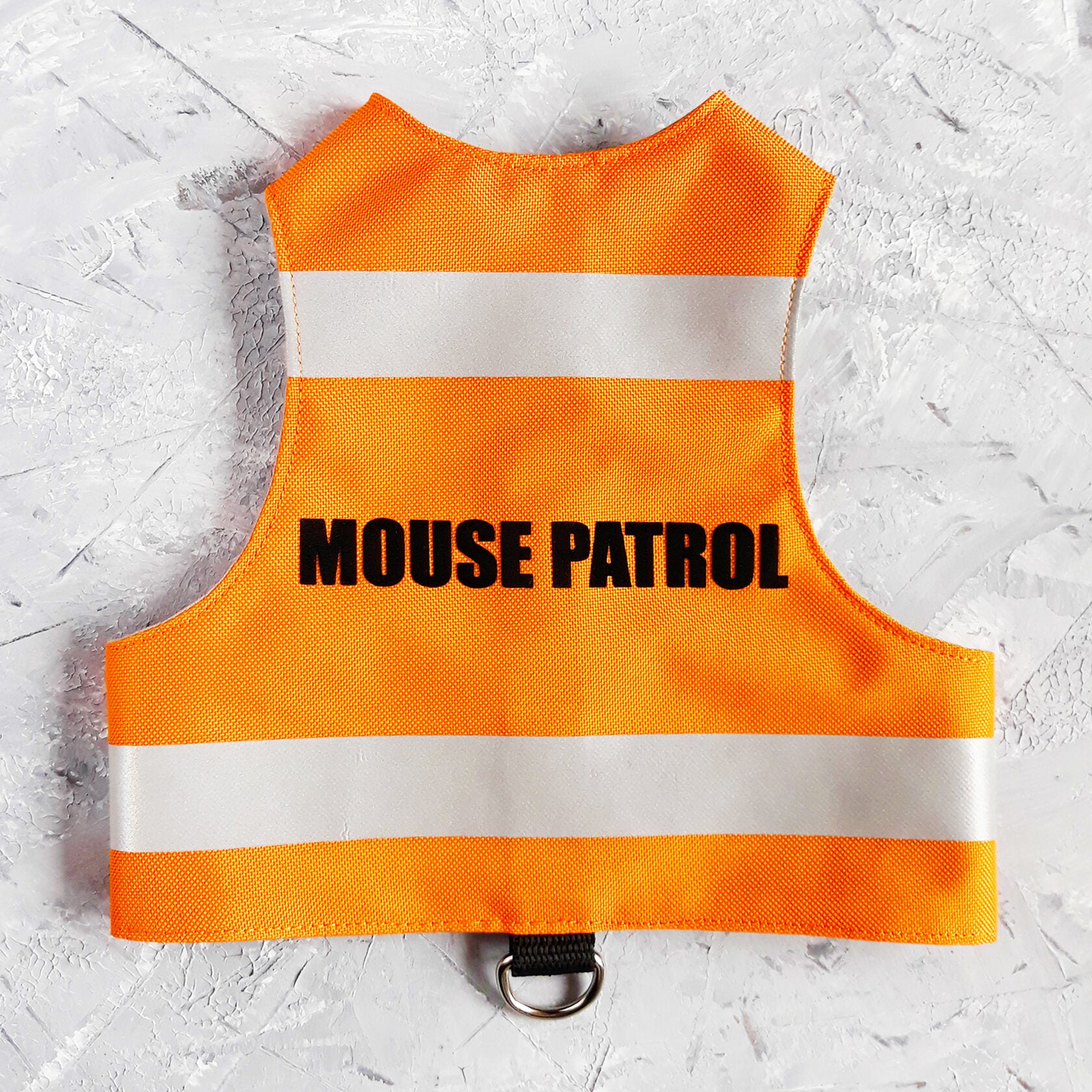A bright orange safety vest with horizontal reflective white stripes and the text "MOUSE PATROL" in black capital letters. A black loop with a silver D-ring is at the bottom.