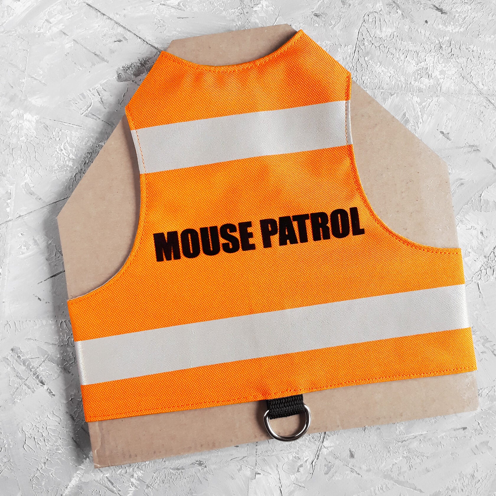 A bright orange safety vest with horizontal reflective white stripes and the text "MOUSE PATROL" in black capital letters. A black loop with a silver D-ring is at the bottom.
