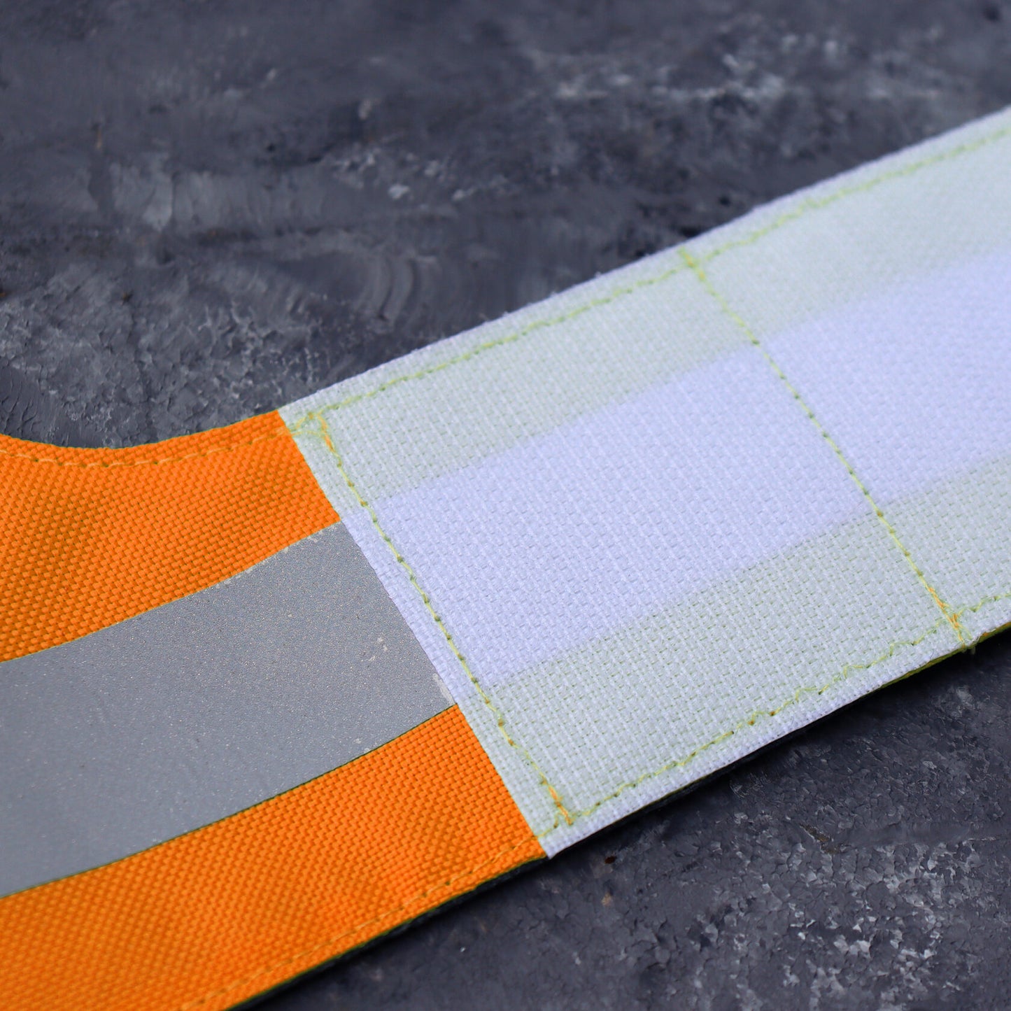 Close-up of a wide reflective silver stripe on a bright orange water-repellent cat harness.