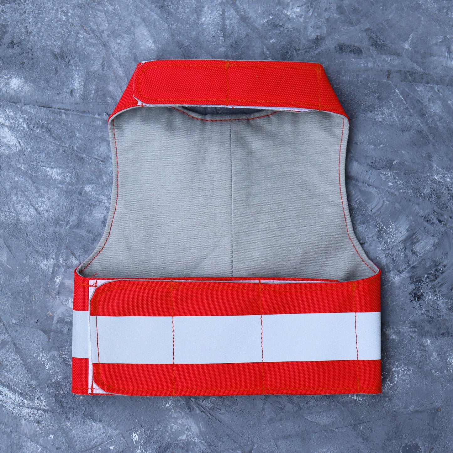 The inside of a bright red water-repellent cat harness showing a plain light grey fabric lining and white Velcro straps.