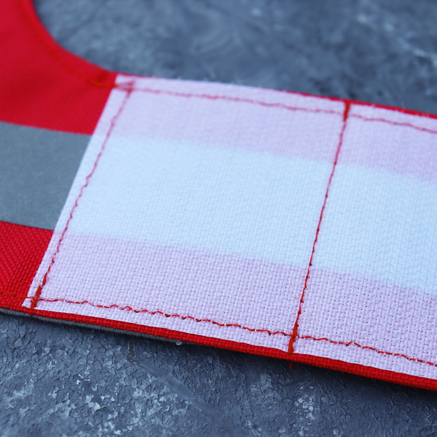 Close-up of a white Velcro strap attached to a bright red water-repellent cat harness with a reflective silver stripe.