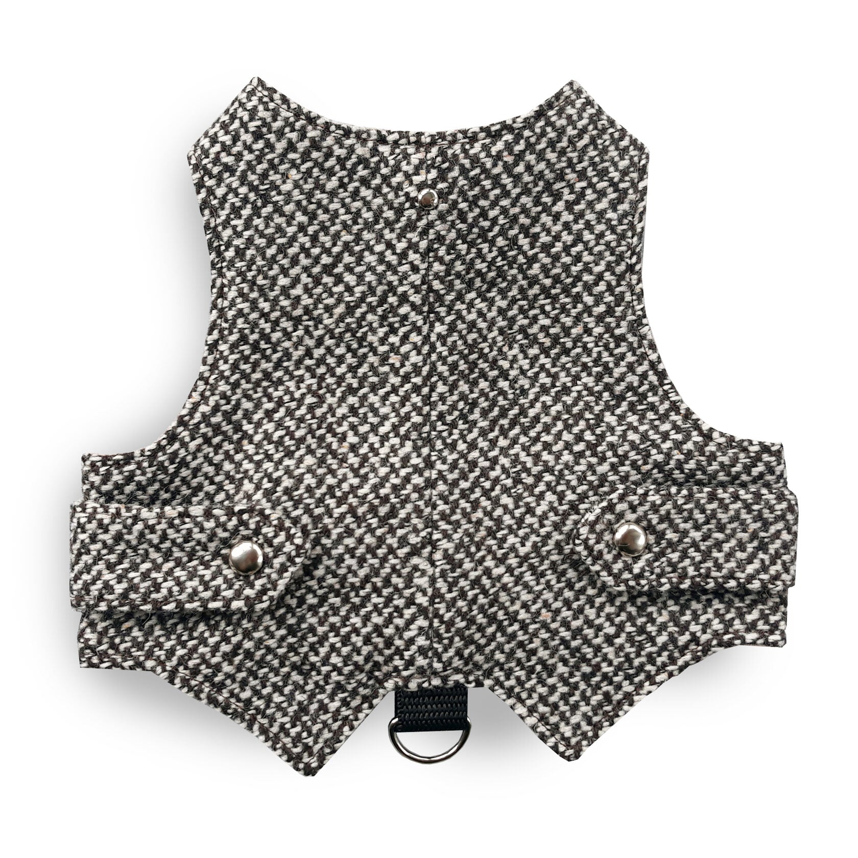 A black and white houndstooth cat harness with silver decorative buttons and a black D-ring, laid flat on a grey surface.