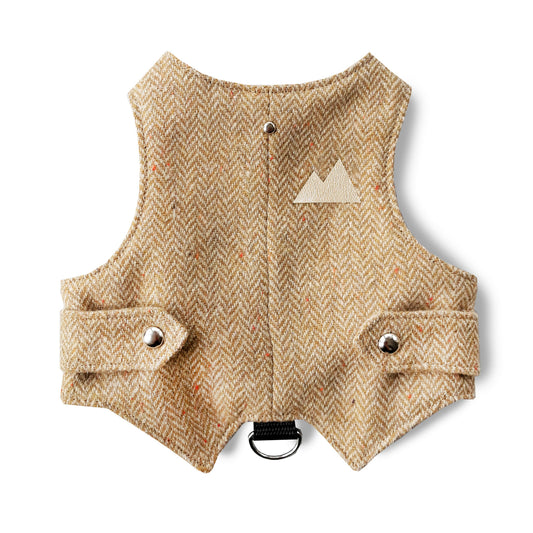 A yellow and brown herringbone tweed cat harness with a light beige leather mountain-shaped patch, silver buttons, and a black D-ring.