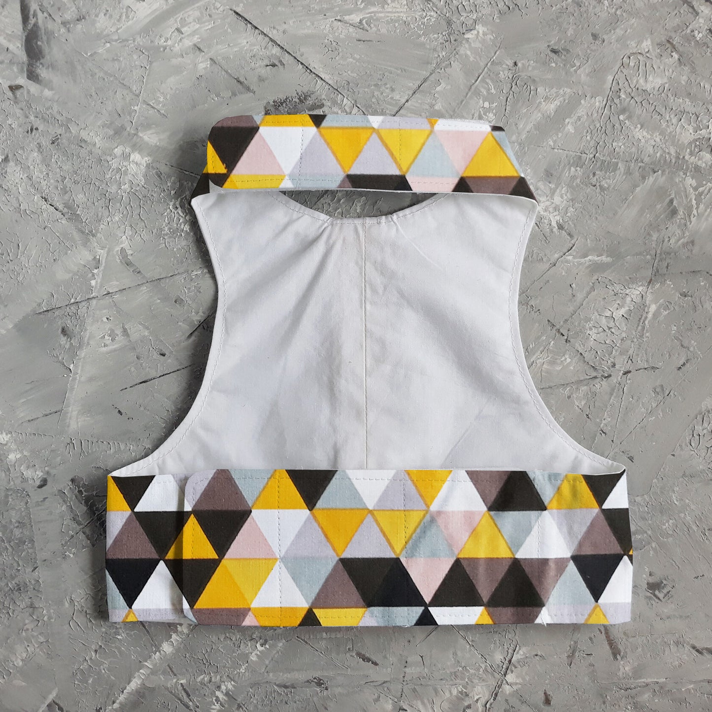 The inside of a cat harness with a geometric triangle pattern in yellow, grey, white, and black on the edges and a plain white fabric lining.