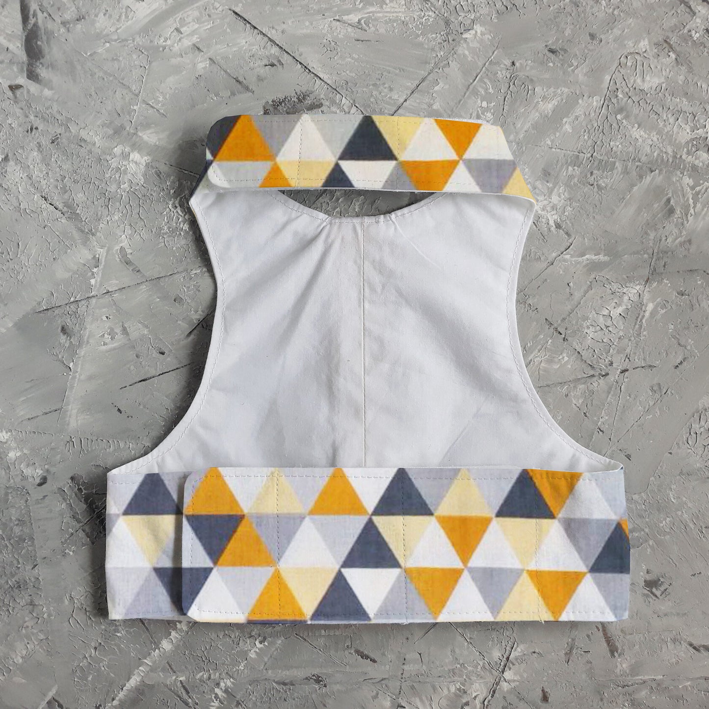 The inside of an escape-proof and safety cat harness with a geometric triangle pattern in yellow, grey, white, and black on the edges and a plain white fabric lining.