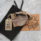 Tweed-style hat for a cat with a small brim and a black ribbon tied in a bow on top, shown on a grey textured surface.