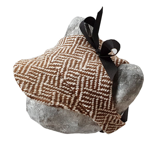 Tweed-style hat for a cat with a small brim and a black ribbon tied in a bow on top, shown on a grey textured surface.