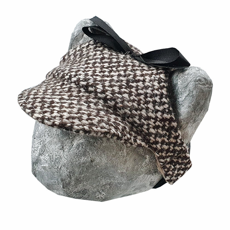 Tweed-style hat for a cat with a small brim and a black ribbon tied in a bow on top, shown on a grey textured surface.
