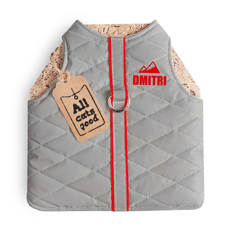 A quilted light grey cat harness with rred trim, a reflective stripe, personalized yellow "DMITRI" text with a mountain icon, and an Allcatsgood tag.