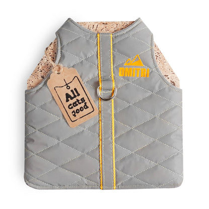 A quilted light grey cat harness with yellow trim, a reflective stripe, personalized yellow "DMITRI" text with a mountain icon, and an Allcatsgood tag.