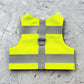 Flat lay of a neon yellow Escape proof cat safety harness with horizontal silver reflective stripes and a grey vertical strap with a D-ring.