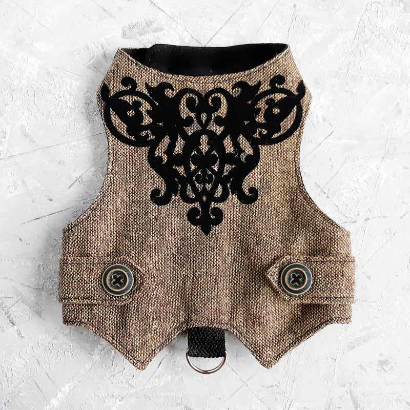 An overhead view of the inner lining of a brown tweed cat harness with a diagonal stripes pattern. The lining is a plain black fabric. A black leash attachment point with a silver D-ring is visible at the bottom.