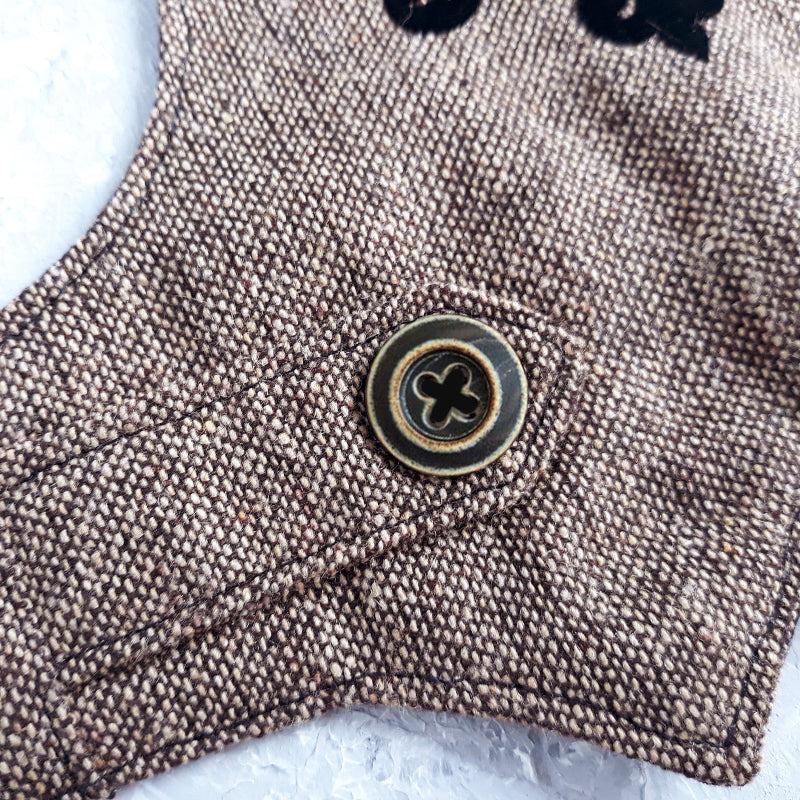 An overhead view of the inner lining of a brown tweed cat harness with a diagonal stripes pattern. The lining is a plain black fabric. A black leash attachment point with a silver D-ring is visible at the bottom.
