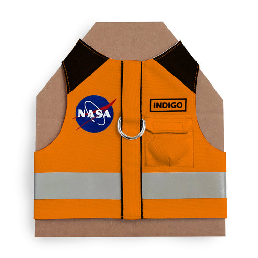 An orange cat harness with black shoulder accents, a NASA logo patch, a reflective silver stripe, and AirTag pocket